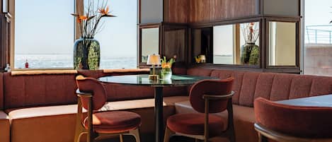 A modern interior with a round table, red upholstered seating, and a view of the sea through large windows.