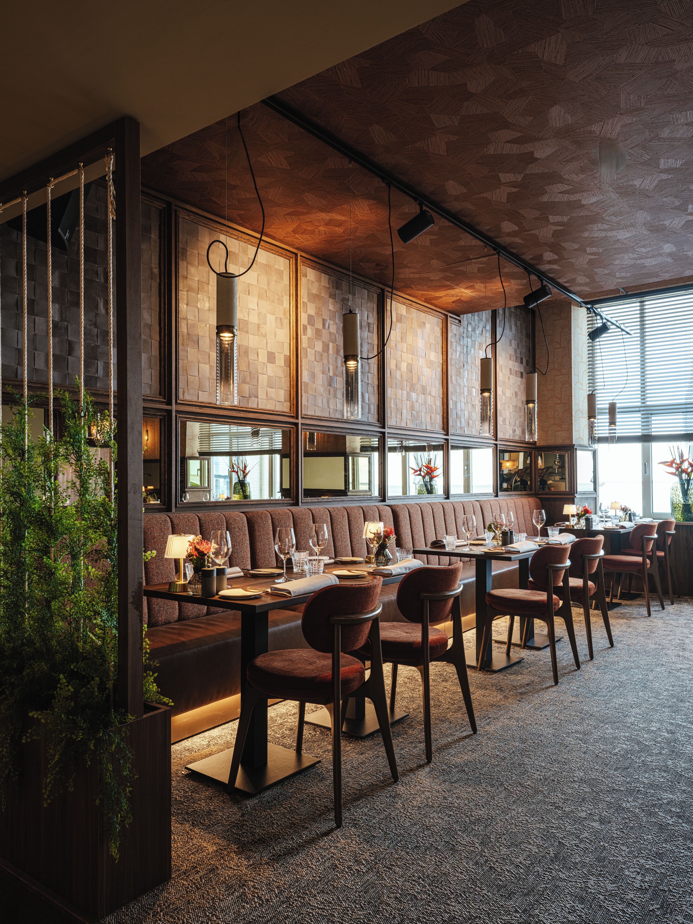A modern restaurant with a long counter, cushioned seating, and a patterned ceiling.