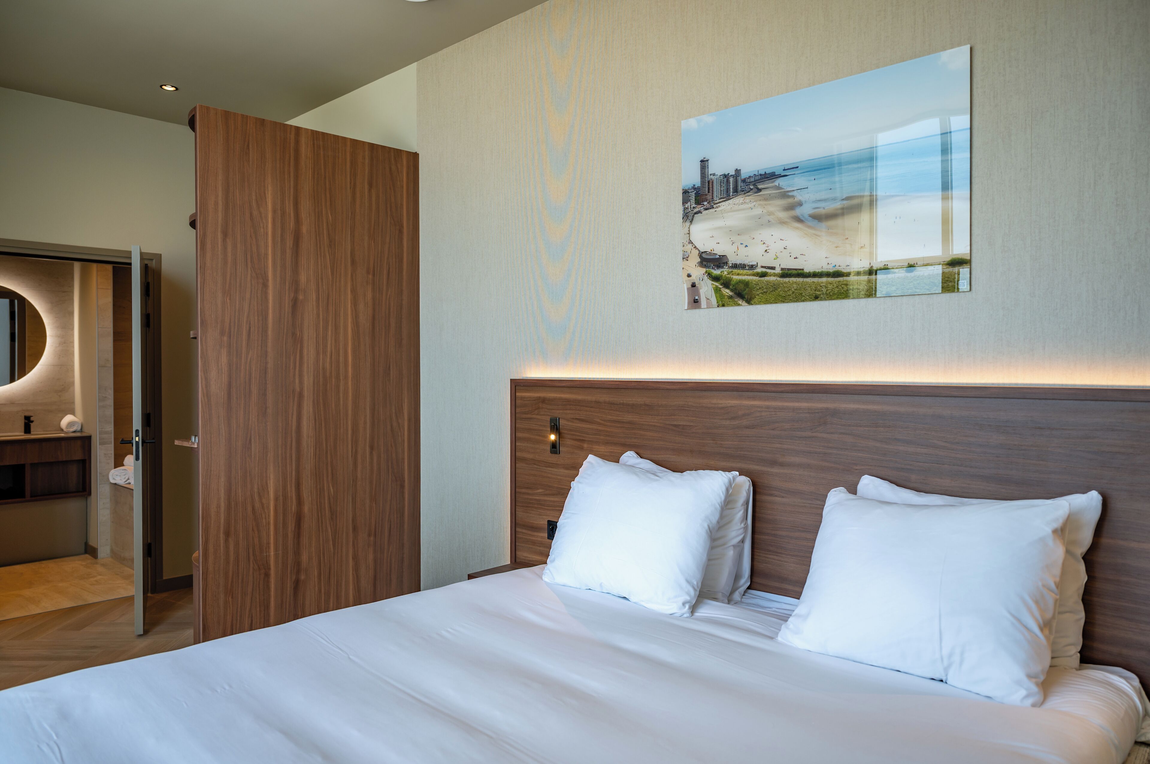 A modern hotel room with a large bed, a wooden headboard, and a cityscape painting on the wall.