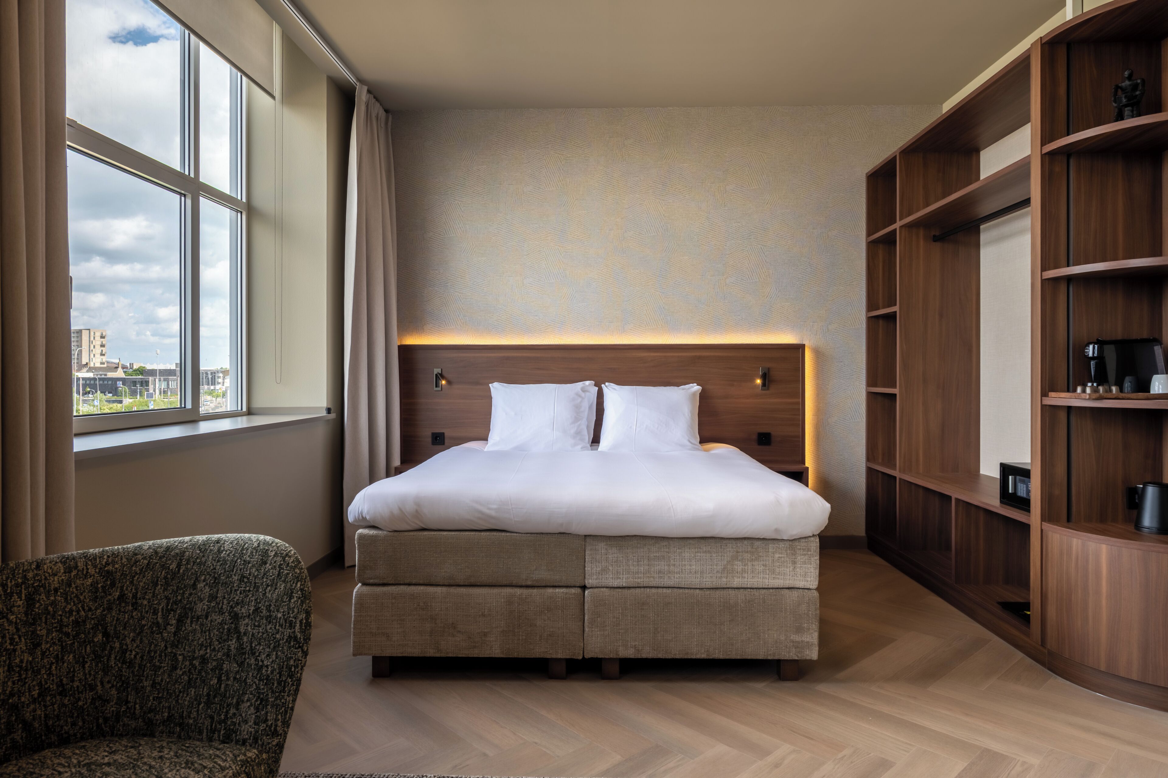 A modern hotel room with a large bed, a seating area, and built-in wooden shelving.
