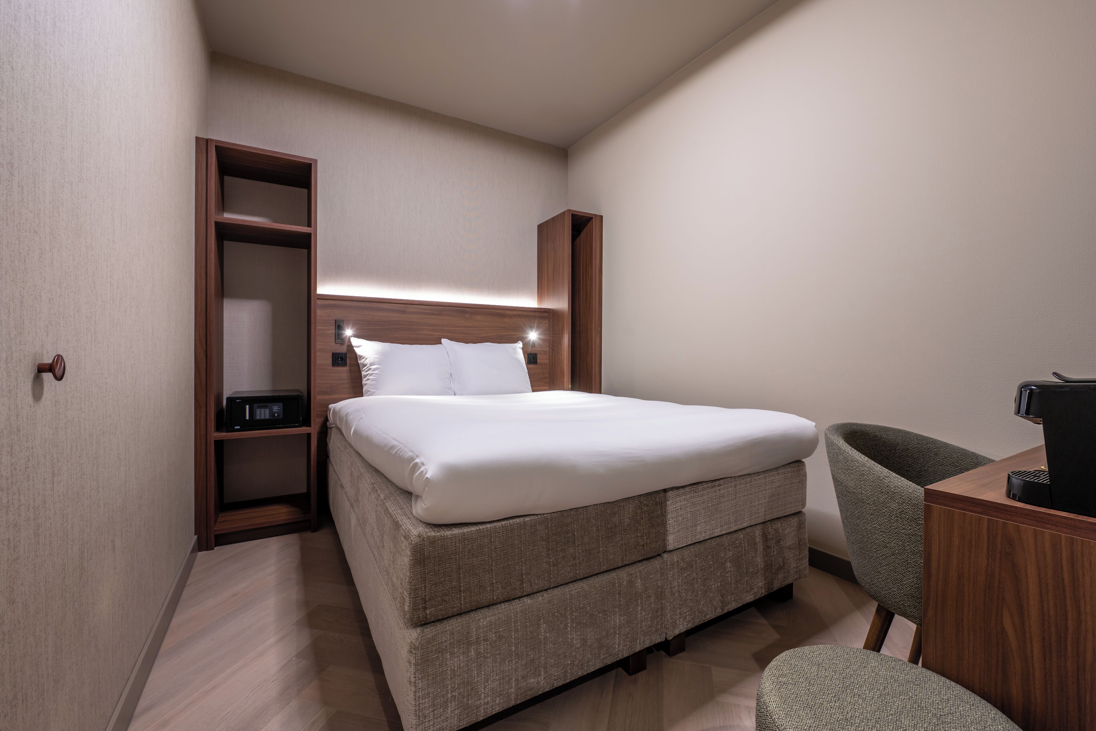 A modern hotel room with a large bed, a built-in wardrobe, a desk, and a chair.