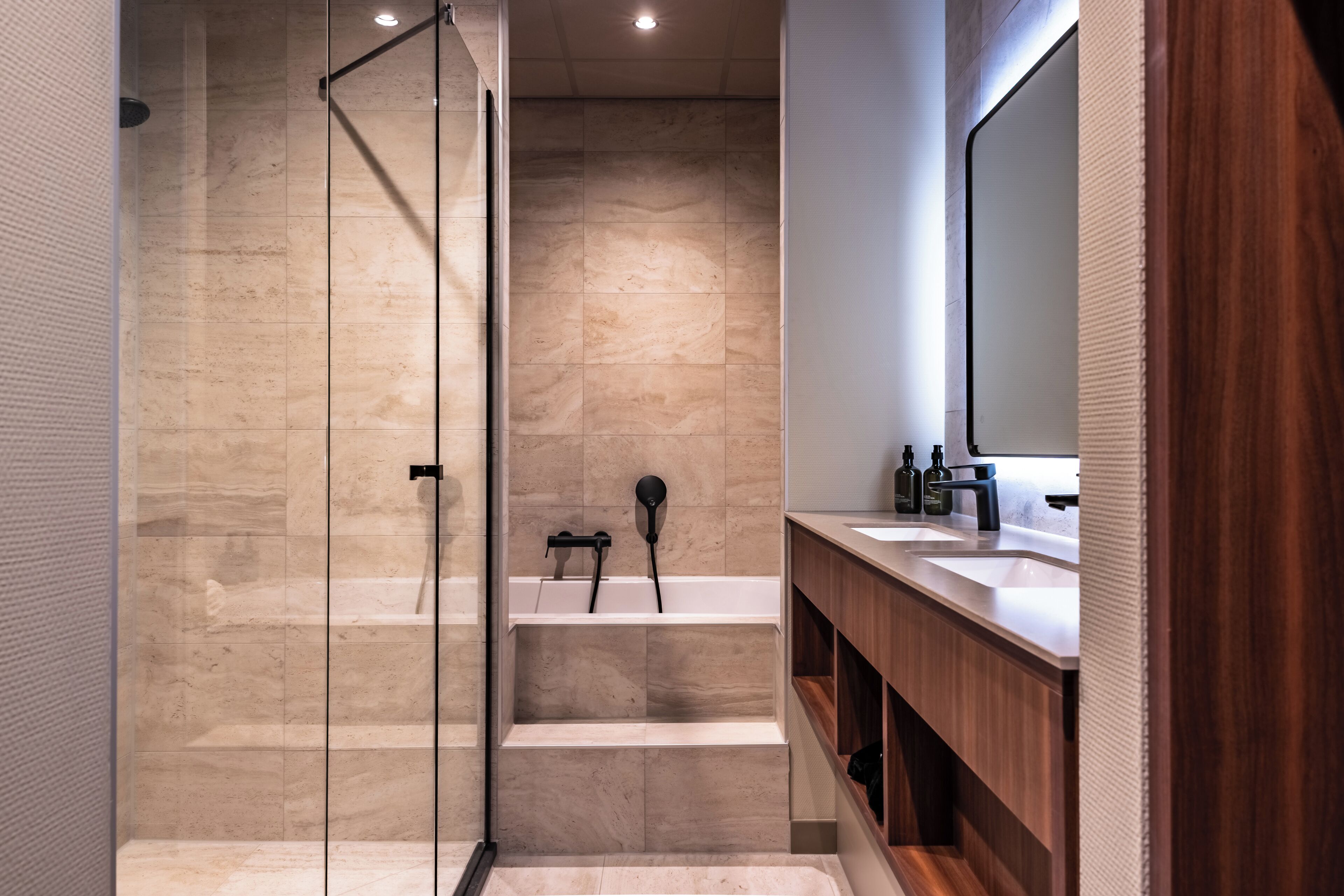 A modern bathroom with a glass-enclosed shower, a wooden vanity with a mirror, and a marble-tiled wall.