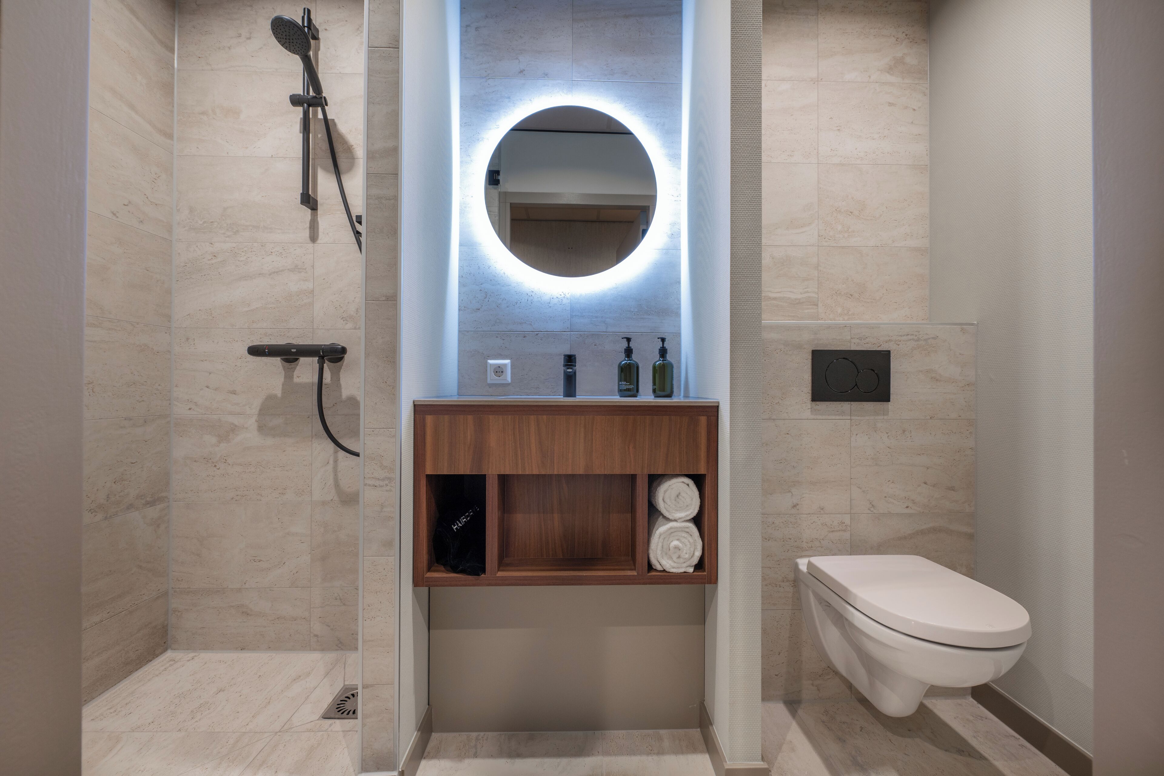 Een moderne badkamer met een douchecabine van glas, een houten wastafelmeubel met spiegel en een toilet.