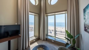 A room with a TV, large windows, a plant, and a painting.