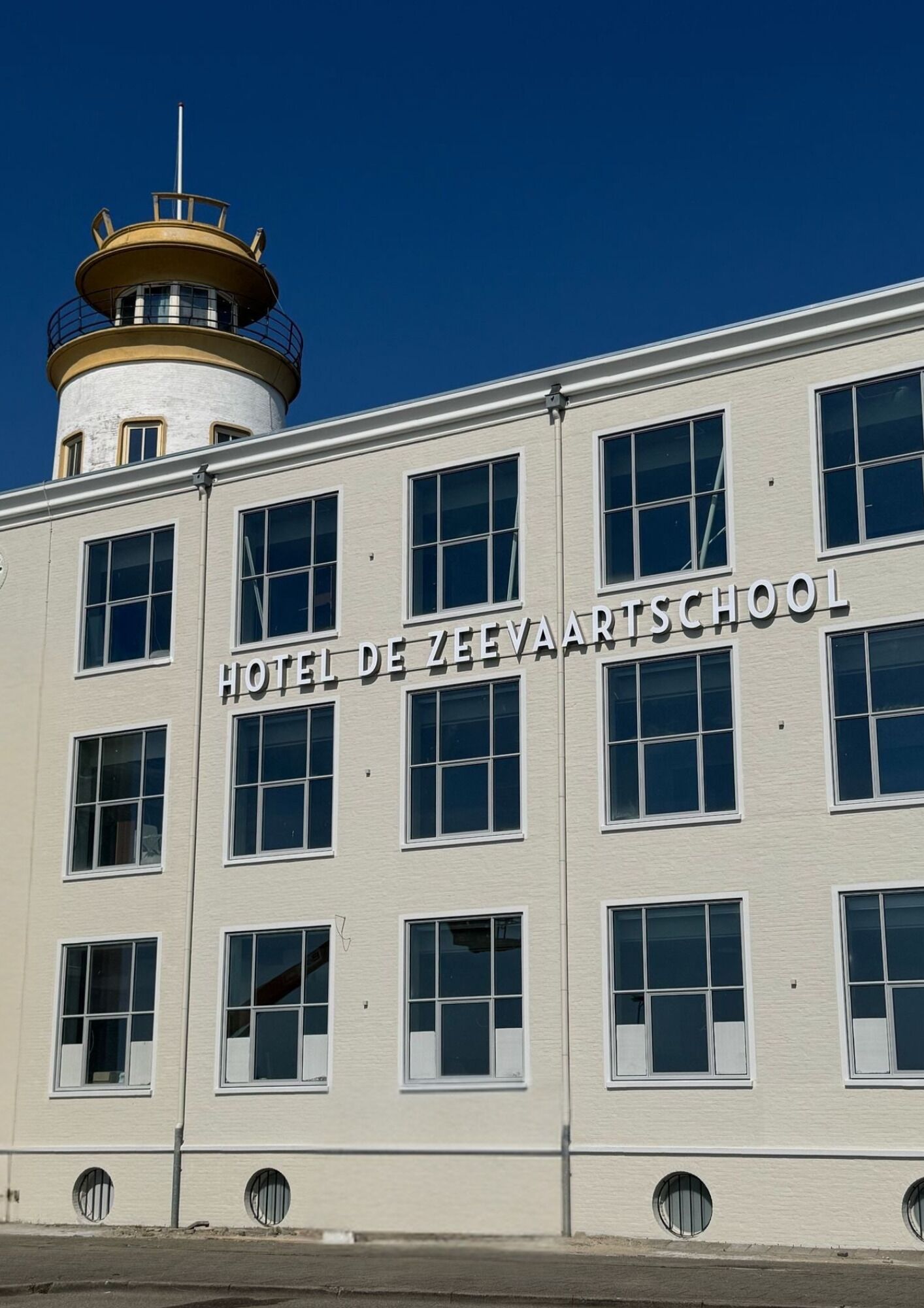 A building with a sign reading "HOTEL DE ZEEVAARTSCHOOL" and a lighthouse structure on top.