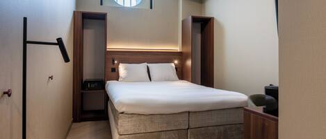 A modern bedroom with a large bed, built-in nightstands, a round window, and a small seating area.