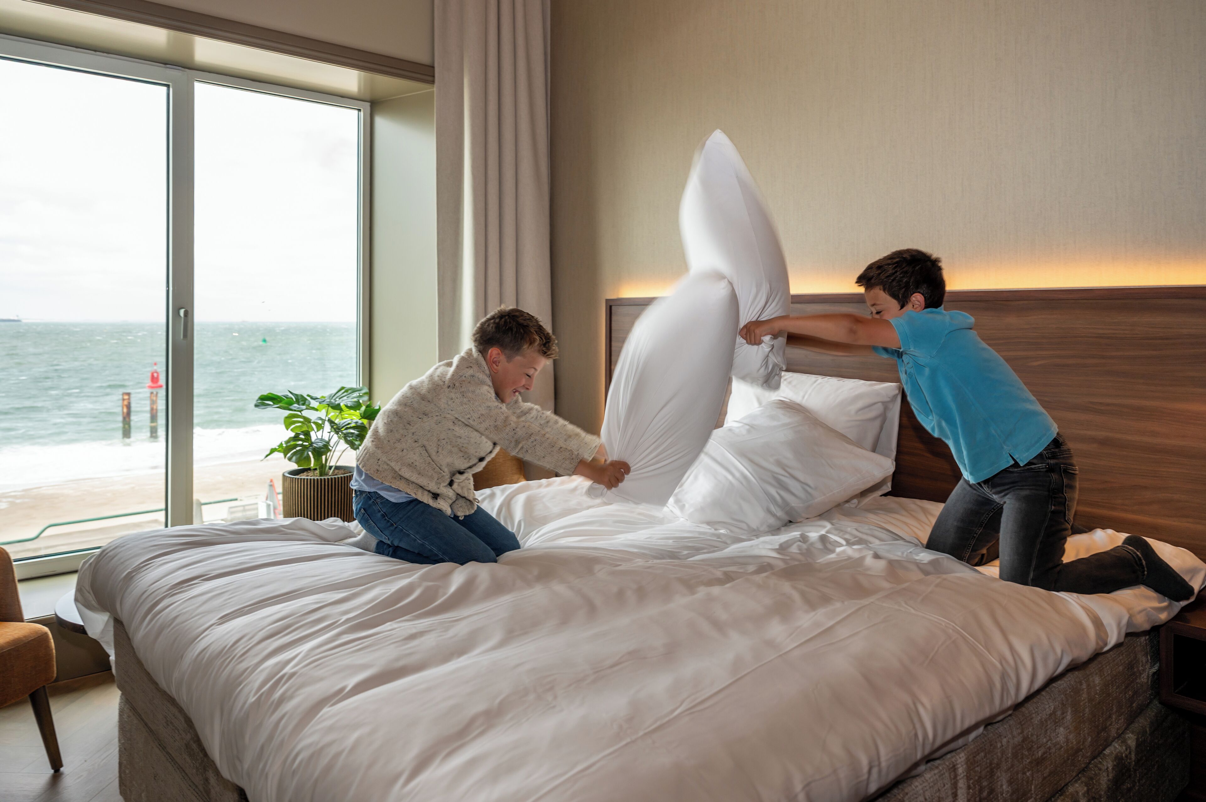 A bed with white bedding and a view of the ocean through large windows.