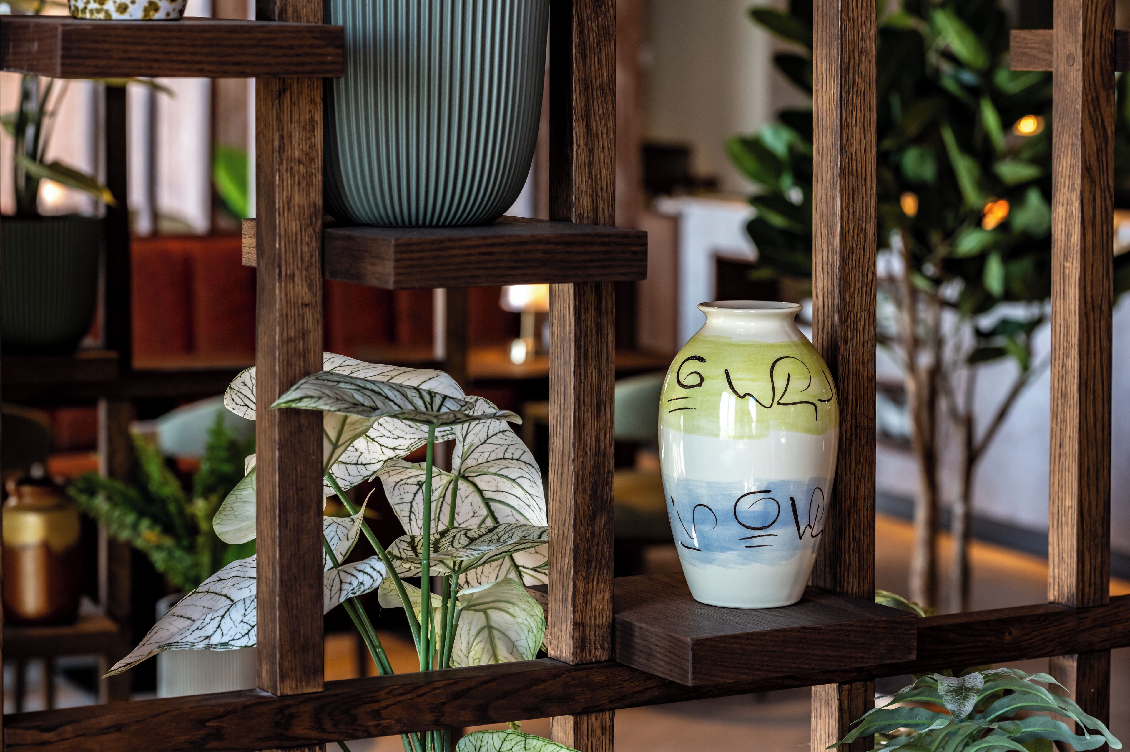A shelf with various decorative items including a blue vase, a white vase with blue and green patterns, and a plant with white leaves.
