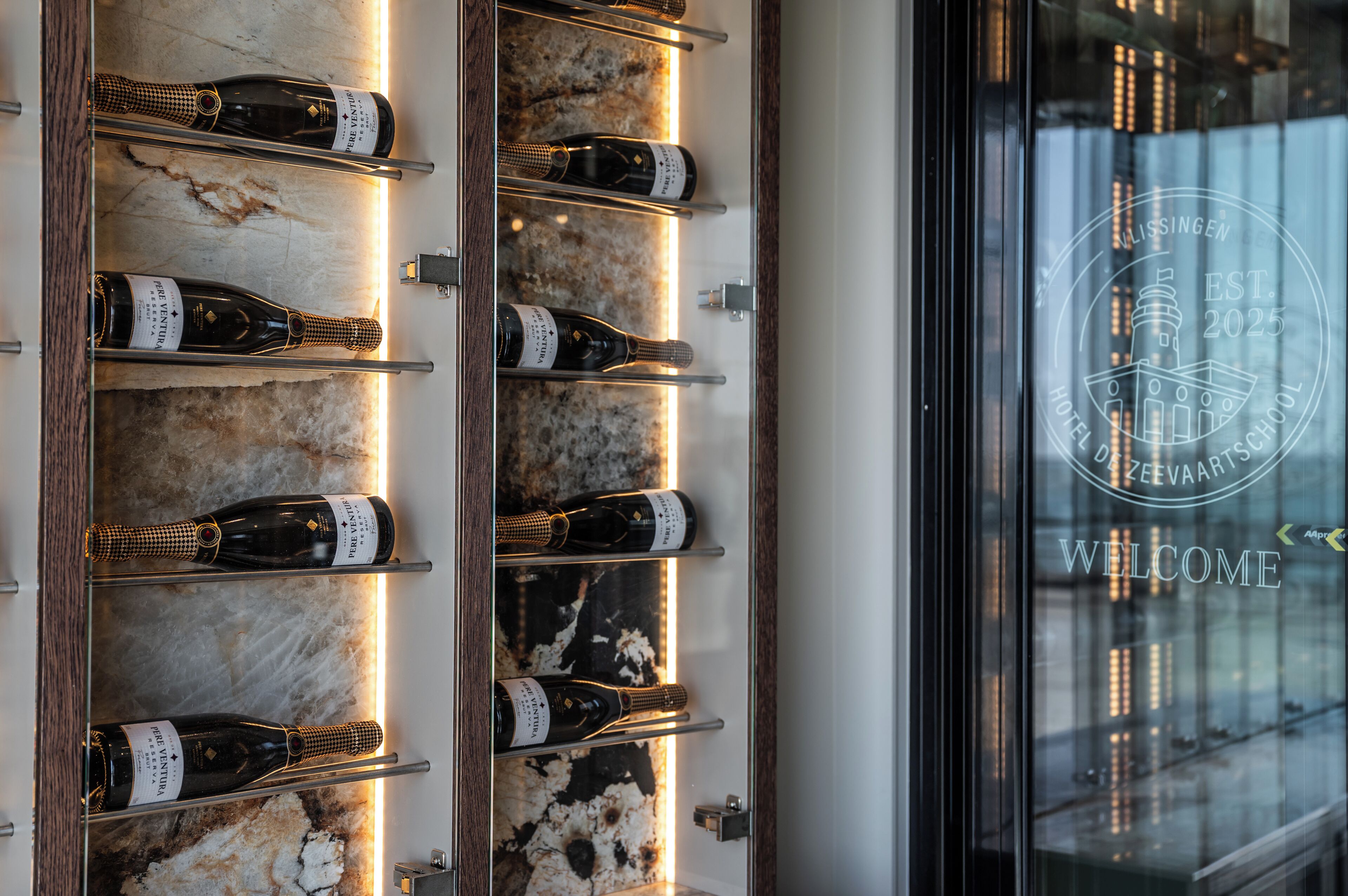 A wall-mounted wine rack with bottles, a marble-like surface, and a welcome sign with a lighthouse emblem.