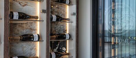 A wall-mounted wine rack with bottles, a marble-like surface, and a welcome sign with a lighthouse emblem.