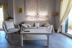 En stue med sofa, stol, sofabord, lampe og et vindue med gardiner.