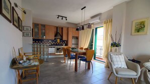 Un coin repas avec une table et des chaises, une cuisine à l’arrière-plan et un espace de vie avec un canapé et un fauteuil.