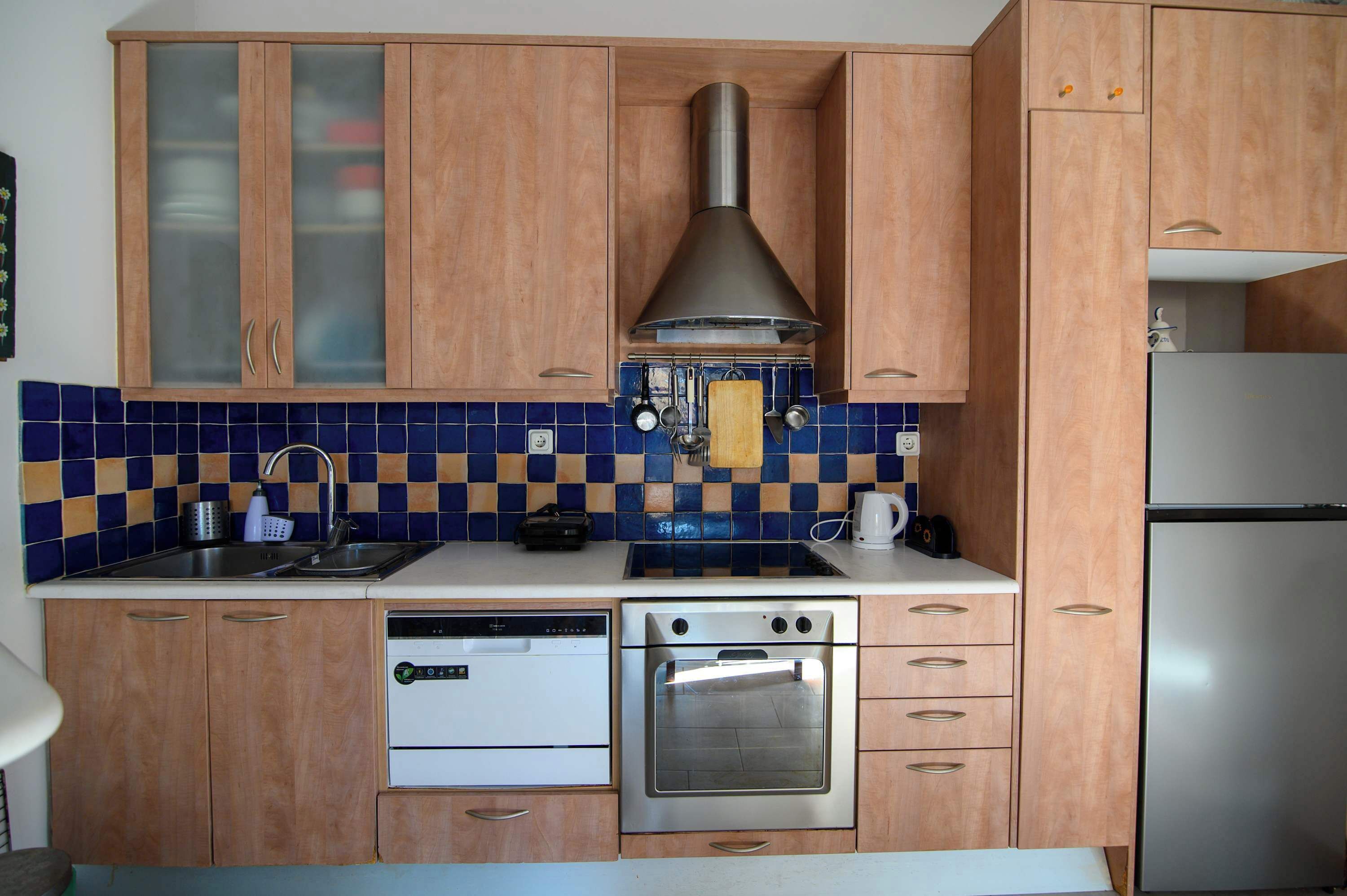 A kitchen with wooden cabinets, a stainless steel range hood, a dishwasher, and an oven.