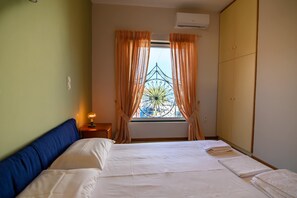 A bedroom with a bed, curtains, a window with a view, an air conditioner, and a bedside lamp.