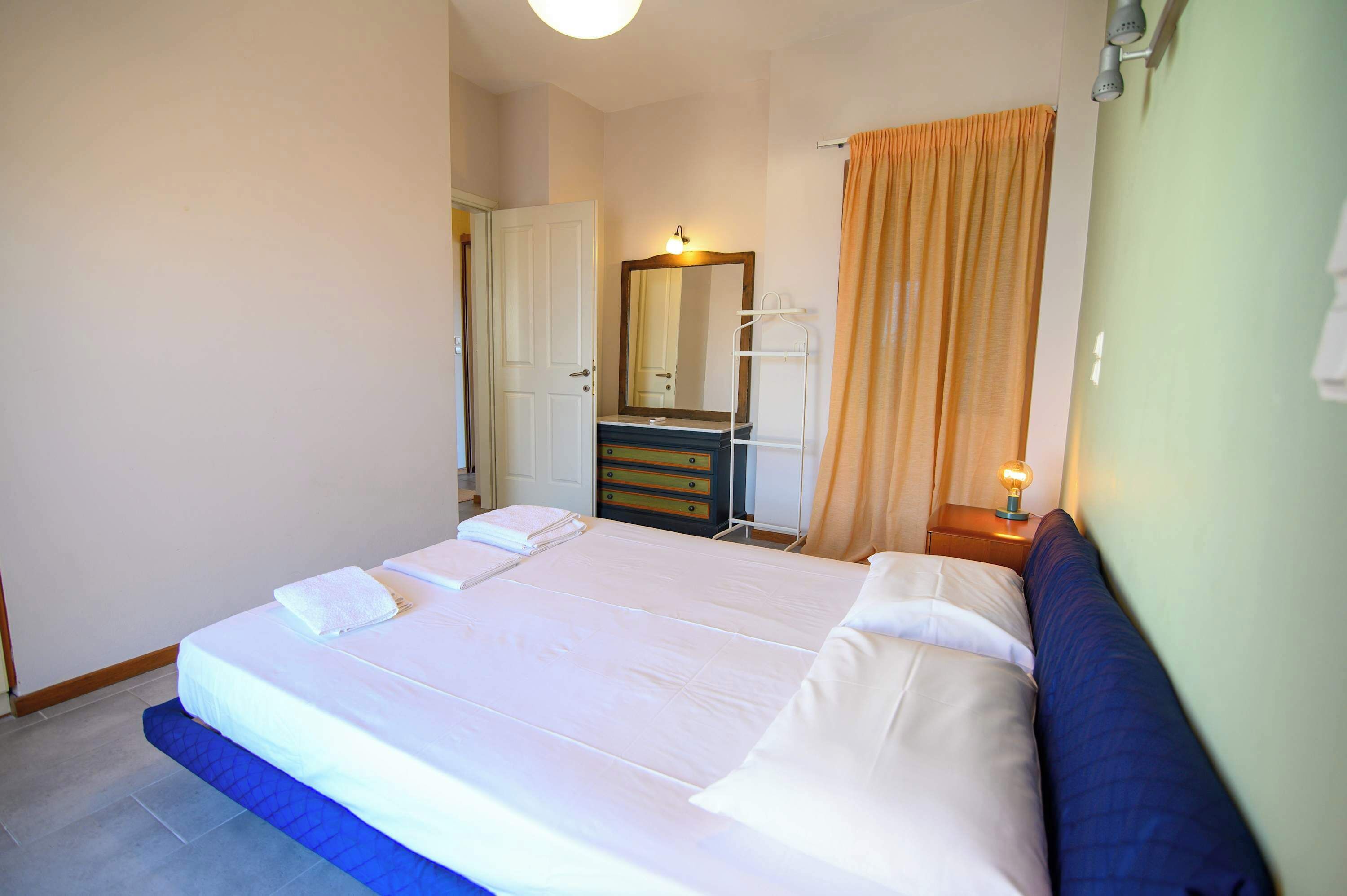 Hotellihuone, jossa on suuri sänky, lipasto, peili ja yöpöytä, jossa on lamppu.