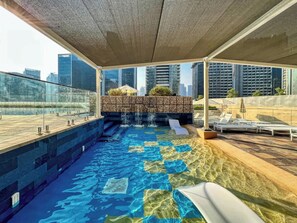 Experience rooftop bliss with a checkered pool, waterfall feature, and submerged loungers. A stylish escape above the city, perfect for sun-soaked relaxation and skyline views.