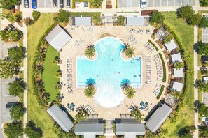Oversigtsbillede af et resort med en central swimmingpool, omgivet af liggestole og palmer.