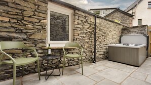 Eine Terrasse mit Steinmauern, zwei Stühlen, einem Tisch und einem Whirlpool.