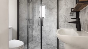 Ein Badezimmer mit einer Duschkabine, einer weißen Toilette und einem weißen Waschbecken mit schwarzem Wasserhahn.