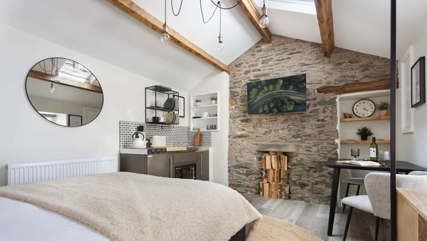 Ein Schlafzimmer mit einem großen Bett, einer Steinsäule, einem Kamin und einer Küchenzeile mit Regalen und einem Wasserkocher.