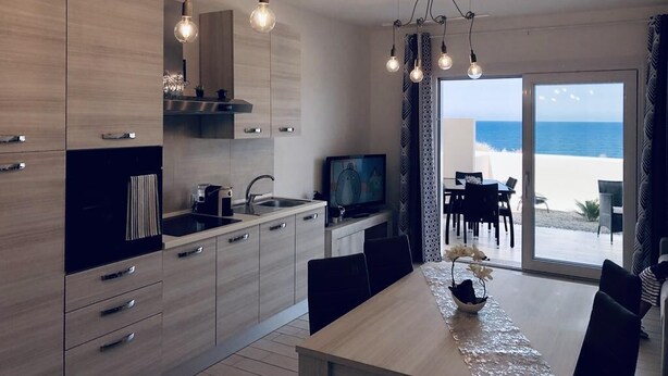 A modern kitchen with a large island, a dining area with a view of the beach, and a sliding glass door leading to the outdoor seating area. - Sunset Luxury house, beachfront with beautiful view within walking distance to the beach! (La Ciaccia)