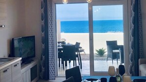 A room with a TV, dining table, chairs, and a view of the beach. - Sunset Luxury house, beachfront with beautiful view within walking distance to the beach! (La Ciaccia)