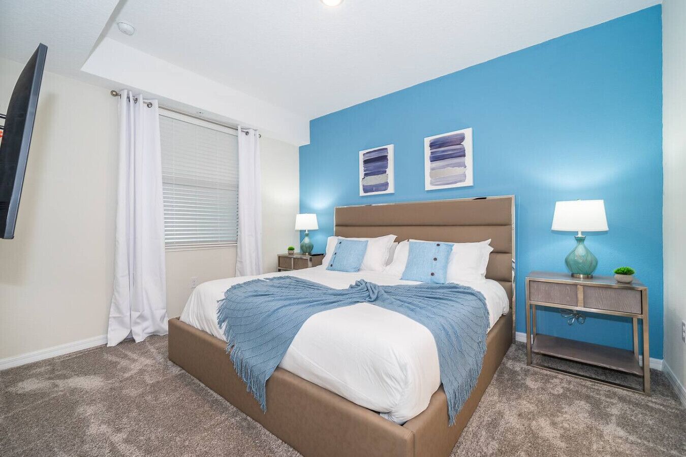 Quarto com cama, duas mesas de cabeceira, televisão e janela com cortinas.
