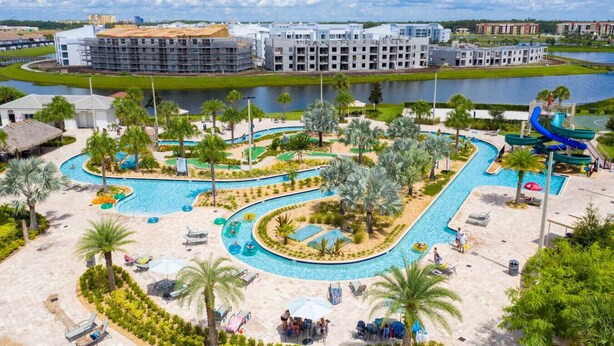 A resort with a large pool area, palm trees, and a water slide. - Modern Condo Near Disney (Kissimmee)