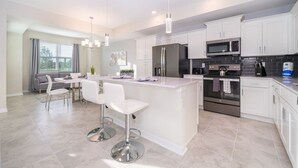 A modern kitchen with white cabinets, stainless steel appliances, and a central island with bar stools. - Modern Condo Near Disney (Kissimmee)
