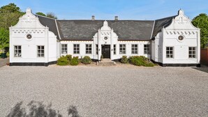 A symmetrical, white building with a central entrance, flanked by two smaller wings, and a gravel driveway.