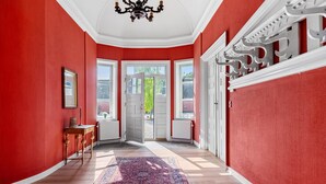 A hallway with red walls, white trim, a chandelier, and a patterned rug.
