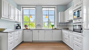 A modern kitchen with white cabinetry, a double sink, and a large window with a view of greenery.