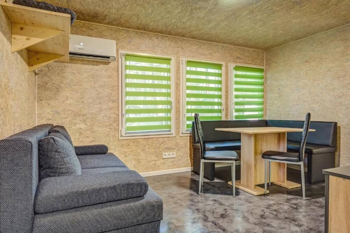 Une pièce de taille modeste, comprenant un canapé, une table à manger avec des chaises et deux fenêtres équipées de stores verts.