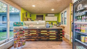 A cafe with a wooden counter, a refrigerator stocked with beverages, and a display of magazines. - Feriendorf Fynnus (Dranske)