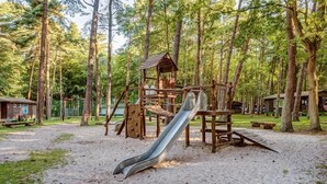 A playground with a slide and climbing structures surrounded by trees. - Feriendorf Fynnus (Dranske)