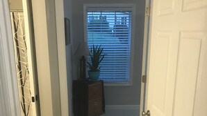 Un couloir doté d’un sol recouvert de moquette, d’une plante en pot, d’une lampe et d’une fenêtre avec des stores.