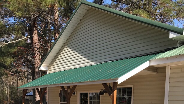 Une petite maison avec un toit végétalisé, une véranda en bois et deux fauteuils à bascule.