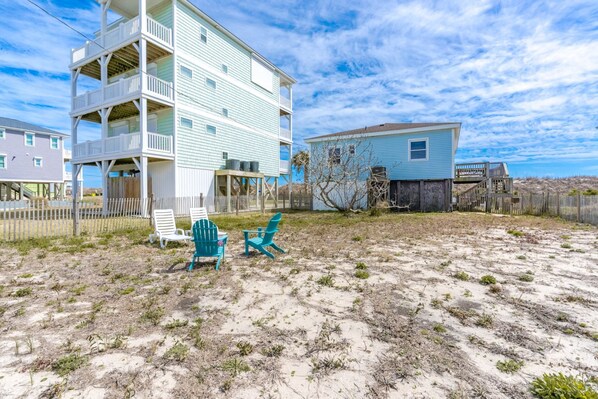 Une propriété située en bord de mer, comprenant un immeuble à plusieurs étages, un espace extérieur aménagé pour s’asseoir et un paysage sablonneux.