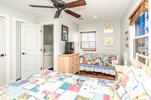 A bedroom with a bed, a dresser, a television, a ceiling fan, and a window with blinds. - Hibiscus Hut - 2 BR Cottage with Panoramic Ocean Views! Dog Friendly (North Topsail Beach)