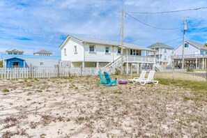 Une propriété située en bord de mer, avec une maison blanche, une terrasse en bois et des chaises de plage.