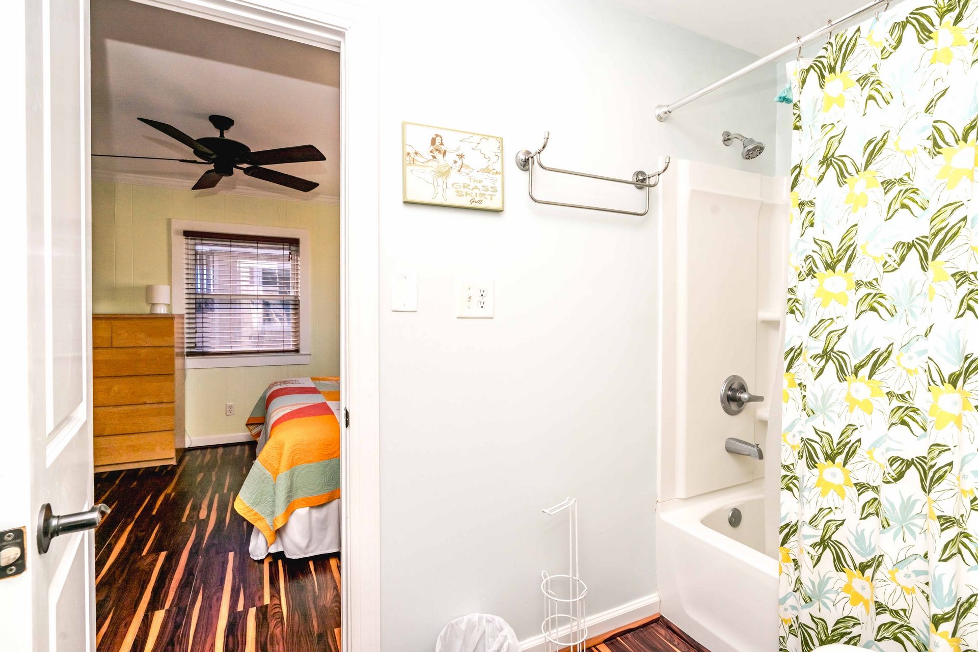 A bathroom with a shower, a toilet, a ceiling fan, and a window with blinds.