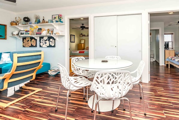 Ein modernes Wohnzimmer mit einem runden Glastisch, weißen Stühlen, einem blauen Sofa und Holzboden.