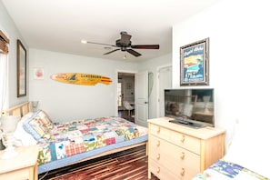 Quarto com cama, ventilador de teto, televisão e decoração com prancha de surf.