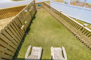 Patio trasero cercado con césped y dos sillas de madera.