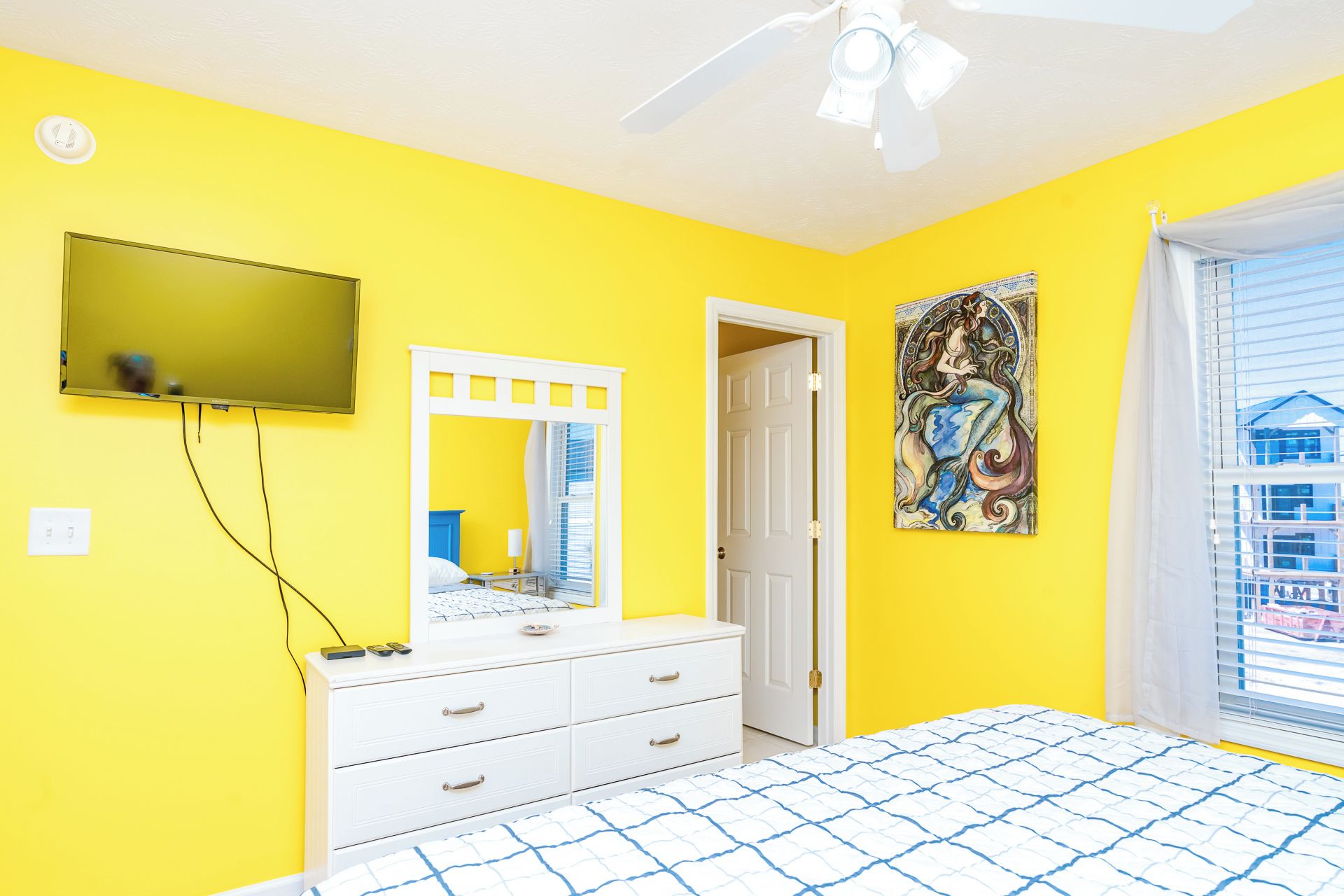 A room with a bed, a dresser, a television mounted on the wall, and a door leading to another room.