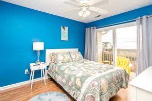 Un dormitorio con cama, mesita de noche, lámpara, ventilador de techo y vistas al exterior.