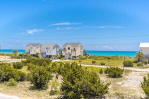 A beachfront property with multiple houses, a clear view of the ocean, and a well-maintained lawn.