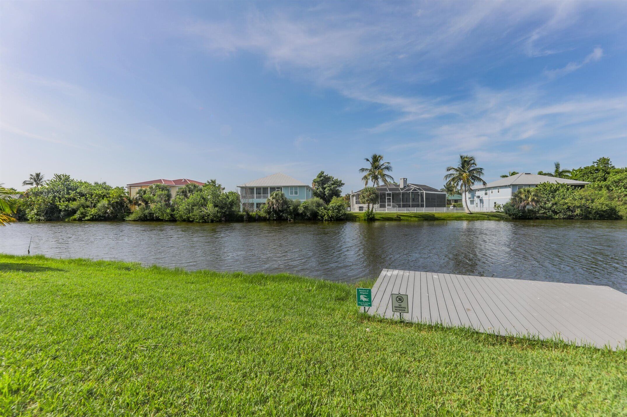 A waterfront property with a grassy area, a wooden dock, and buildings with red roofs.