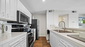 Una cocina moderna con armarios blancos, electrodomésticos de acero inoxidable, encimera negra y suelo de madera.