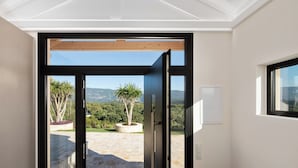Une porte ouverte donnant sur un balcon d’où l’on peut admirer un jardin aménagé et des montagnes lointaines.